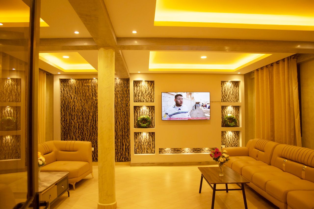 A hotel room with a large flat-screen TV mounted on the wall, a sofa, a coffee table, and decorative wall panels.