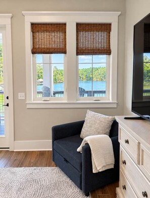 A room with a dark blue sofa, a white dresser, and a view of a lake through two windows with bamboo blinds. - NEW RENTAL! - The Eagle's Landing on Lake Martin (Jackson's Gap)