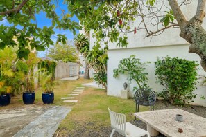A patio area with a table and chairs, surrounded by potted plants and a white wall. - Maré 2BR | Near Ocean Park Beach + Laundry (San Juan)