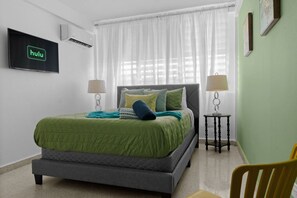 Ein Schlafzimmer mit einem Bett, zwei Nachttischen inklusive Lampen, einem an der Wand befestigten Fernseher und einem Sessel.