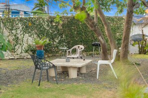 Ein Sitzbereich im Freien mit Tisch und Stühlen, umgeben von einer Hecke und einem Zaun.