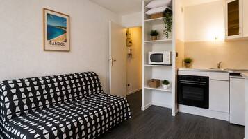 A compact living space with a black and white patterned sofa, a kitchenette with white cabinets, a microwave, and a small potted plant.