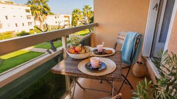 A balcony with a table set for two, a bowl of fruit, two cups, and a basket.