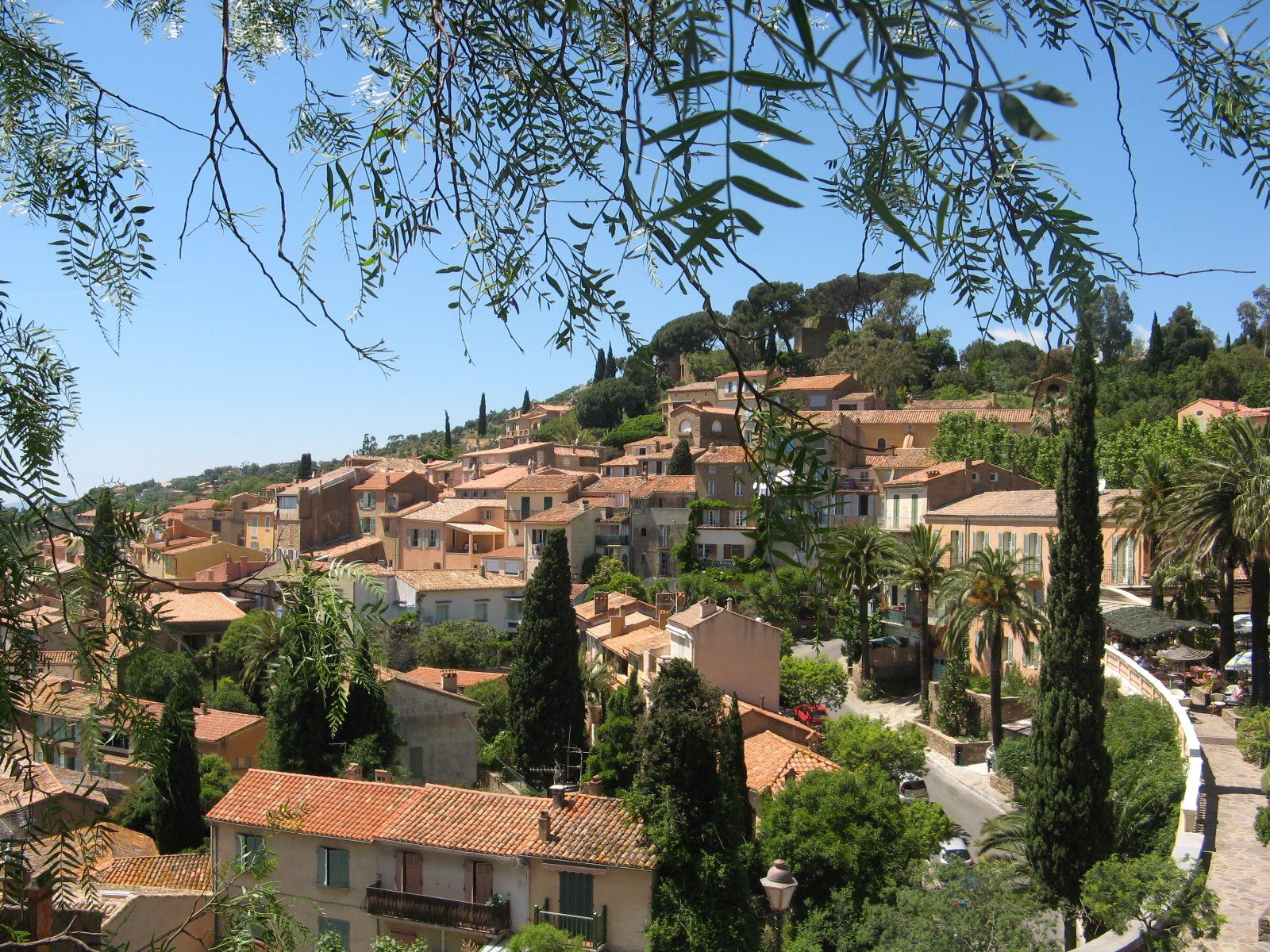 Une ville située sur une colline, avec des bâtiments aux toits de tuiles rouges, une végétation luxuriante et un ciel d’un bleu limpide.