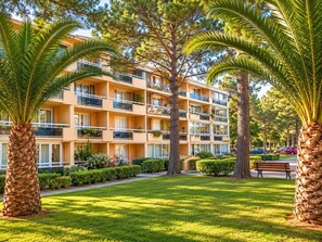 Un hotel a più piani con balconi, immerso in prati curati e palme.