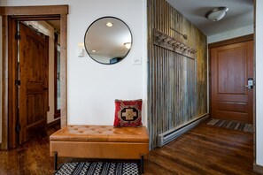 A hallway with a wooden bench, a round mirror, and a rustic wall panel. - Bright Mountain Modern Condo @ The Lodge in Steamboat Springs! (Steamboat Springs)