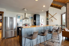 A modern kitchen with stainless steel appliances, a wooden island with bar stools, and a large window providing natural light. - Bright Mountain Modern Condo @ The Lodge in Steamboat Springs! (Steamboat Springs)