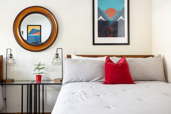 Een netjes ingerichte hotelkamer met een bed, een nachtkastje met een lamp, een kleine potplant en een ingelijst beeld aan de muur.