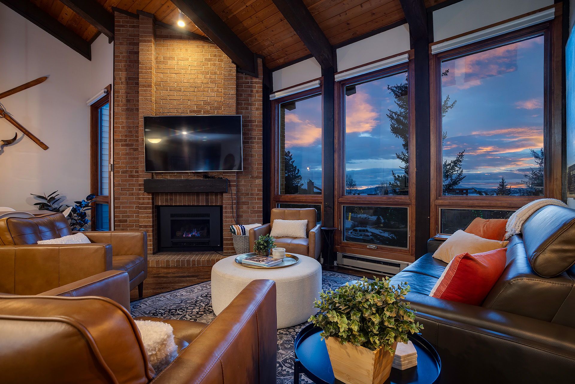 A cozy living room with leather sofas, a fireplace, and large windows offering a scenic view.