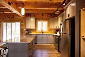 A modern kitchen with wooden cabinets, stainless steel appliances, and a large island with bar stools. - Cozy Cabin Cottage on Big Gull Lake Waterfront (North Frontenac)