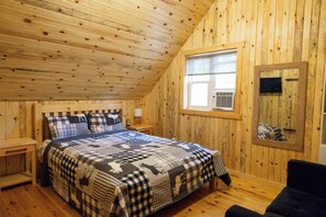 A cozy wooden cabin bedroom with a bed, a nightstand, a window, and a television mounted on the wall. - Cozy Cabin Cottage on Big Gull Lake Waterfront (North Frontenac)