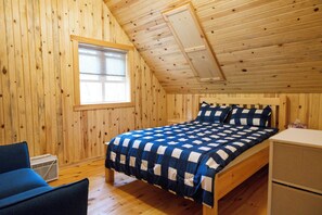 A wooden-paneled room with a bed, a chair, a desk, and a window. - Cozy Cabin Cottage on Big Gull Lake Waterfront (North Frontenac)