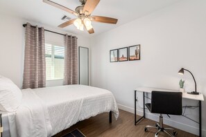 A bedroom with a bed, a desk, a chair, a ceiling fan, and a window with curtains. - Bright 2BR Phoenix Home | Near RoRo + Parking (Phoenix)
