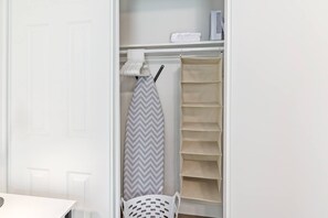 Organized closet with hangers, shelving, a laundry basket, iron, and ironing board—especially convenient for longer stays. - Bright 2BR Phoenix Home | Near RoRo + Parking (Phoenix)