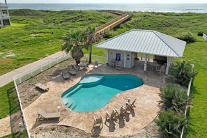 A pool area with a curved pool, lounge chairs, and a covered seating area. - Cici's Hideaway (Port Aransas)