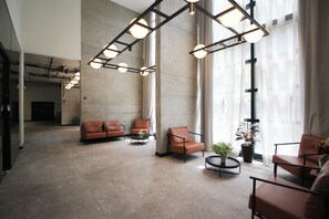 Eine geräumige Lobby mit hoher Decke, großen Fenstern und einer modernen Sitzgruppe, darunter Sofas und Sessel.