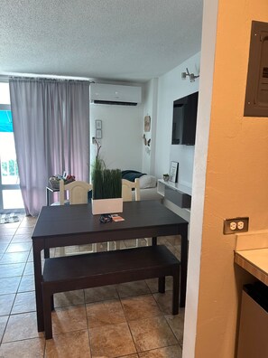 Un salon moderne avec une table en bois foncé, un banc, une plante en pot et un téléviseur à écran plat fixé au mur.