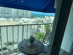 A balcony with a view of a cityscape, a potted plant, and a blue awning. - Saint Tropez Great Apartment & Location (Carolina)