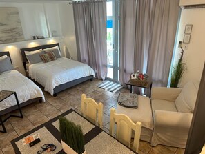 A hotel room with two beds, a sofa, a small table, and a chair. There is a window with curtains, a door, and a wall-mounted phone. - Saint Tropez Great Apartment & Location (Carolina)
