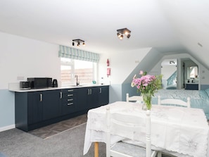 A compact kitchen with dark cabinets, a white countertop, and a window with a striped valance. - Merlins Hideaway (Dawlish)