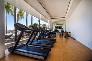 A gym with treadmills aligned along a wall with large windows, overlooking a cityscape. - Pier 57 - Luxurious Condo in Zona Romantica (Puerto Vallarta)