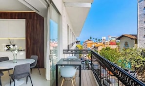 A balcony with a dining table and chairs, a vase with flowers, and a view of the cityscape. - Pier 57 - Luxurious Condo in Zona Romantica (Puerto Vallarta)