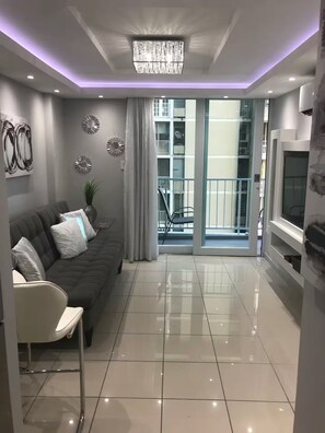 Ein modernes Wohnzimmer mit einer Couch, einem Sessel, einem Fernseher und einem Balkon mit Geländer.