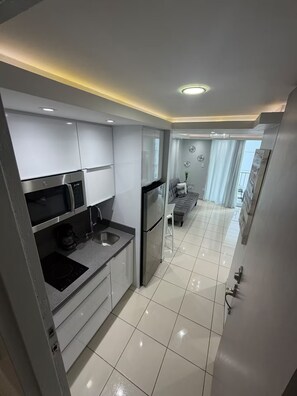 Eine moderne Küche mit integriertem Mikrowellenherd, einem Edelstahlkühlschrank und einem grauen Sofa im angrenzenden Wohnbereich.