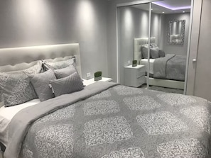 Ein modernes Schlafzimmer mit einem großen Bett, einem Nachttisch, einem Spiegel und einem Kleiderschrank.