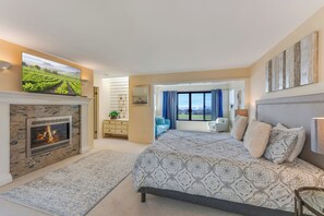 A bedroom with a fireplace, a large bed, a TV, and a view of the countryside. - Once Upon A Tide, by Vinifera Homes (Bodega Bay)