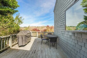 A deck with a covered grill, a table, and chairs, overlooking a hilly landscape. - Once Upon A Tide, by Vinifera Homes (Bodega Bay)