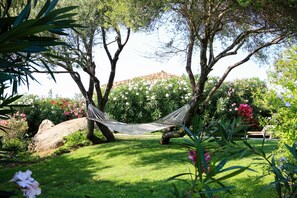 A hammock tied between two trees in a lush garden with a stone wall in the background. - LuxRent Villa Smeralda Pool and Beach (San Teodoro)