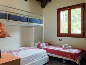 A room with bunk beds, a small table, a lamp, a window with blinds, and a bed with a patterned bedspread. - LuxRent Villa Smeralda Pool and Beach (San Teodoro)