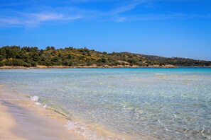 A beach with clear shallow waters, a sandy shore, and a hilly landscape with vegetation in the background. - LuxRent Villa Smeralda Pool and Beach (San Teodoro)