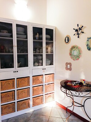 A room with a white cabinet containing glassware and dishes, wicker baskets, and a table with a decorative plate and a small mirror. - LuxRent Villa Smeralda Pool and Beach (San Teodoro)