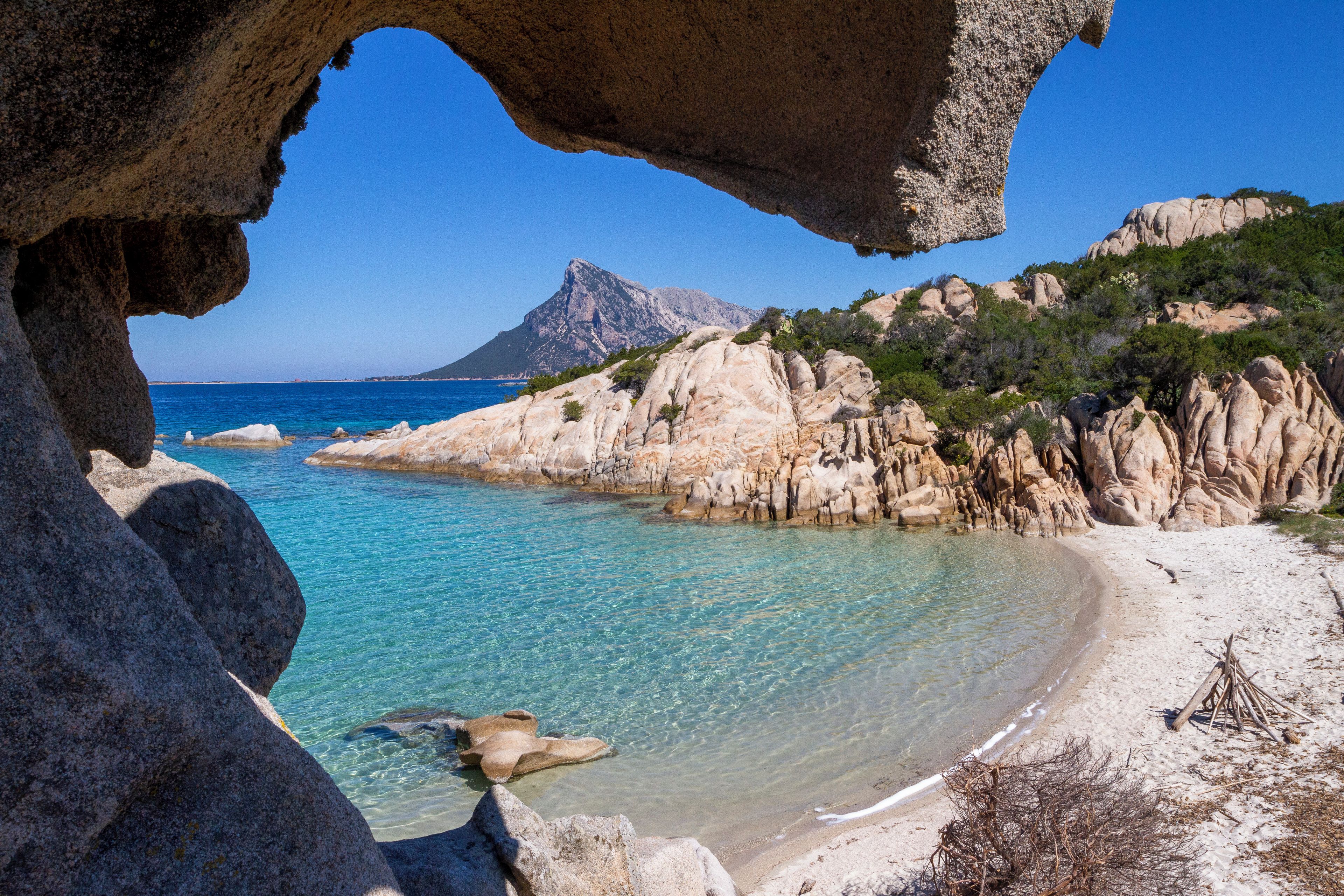 A coastal landscape with clear turquoise waters, rocky formations, and a distant mountain.