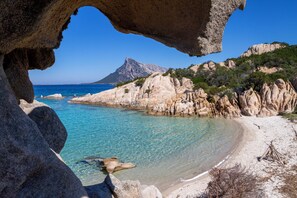 Un paysage côtier caractérisé par des eaux turquoise limpides, des formations rocheuses et une chaîne de montagnes visible au loin.