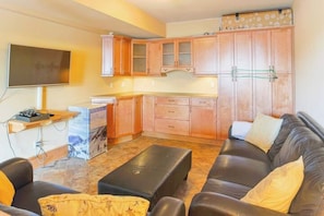A compact living space with a sofa, a coffee table, a TV, and wooden cabinets. - 4-storey Cedar Ridge townhouse - Hot tub - BBQ (Fernie)