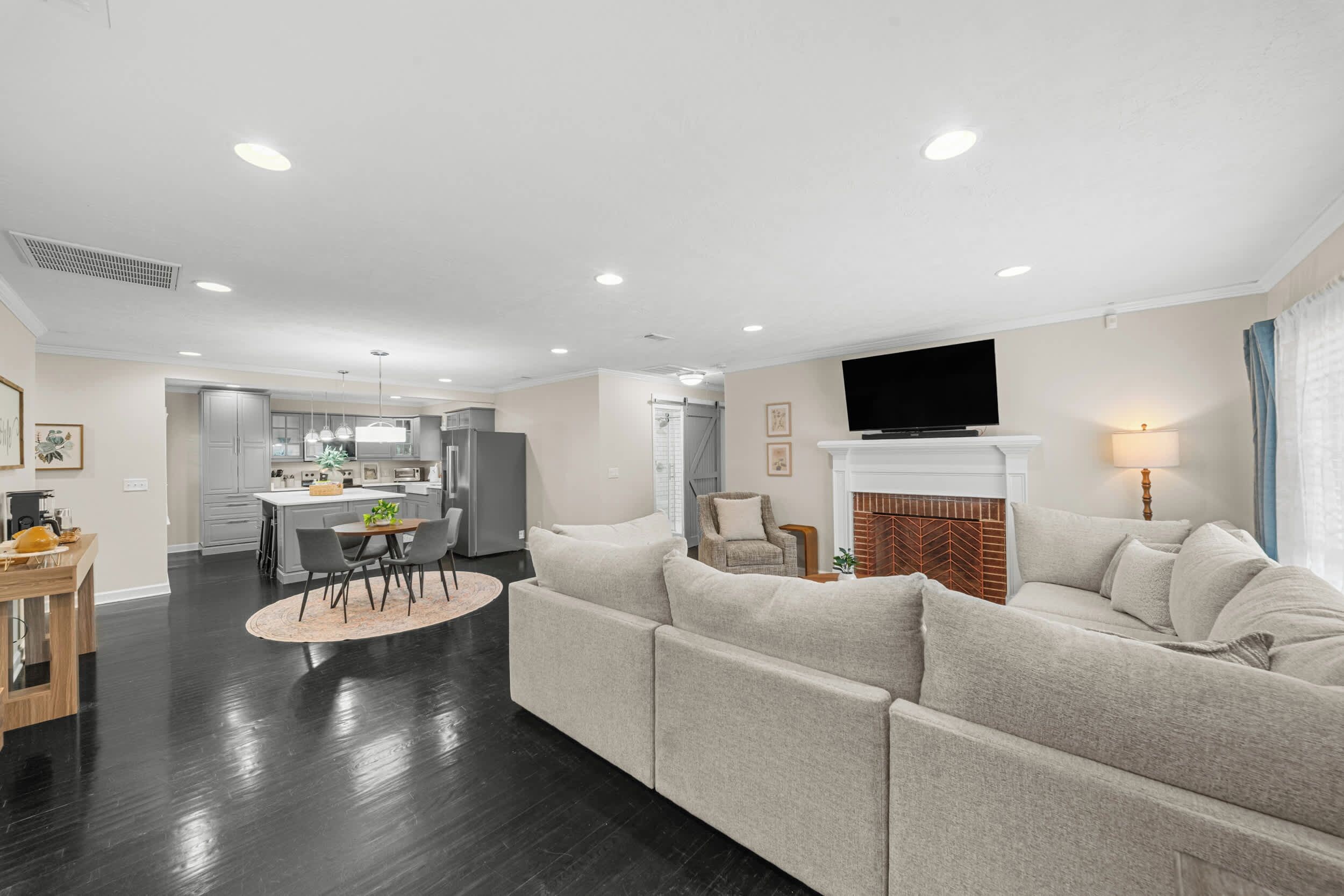 A modern living room with a large sofa, a dining area, and a kitchen in the background.