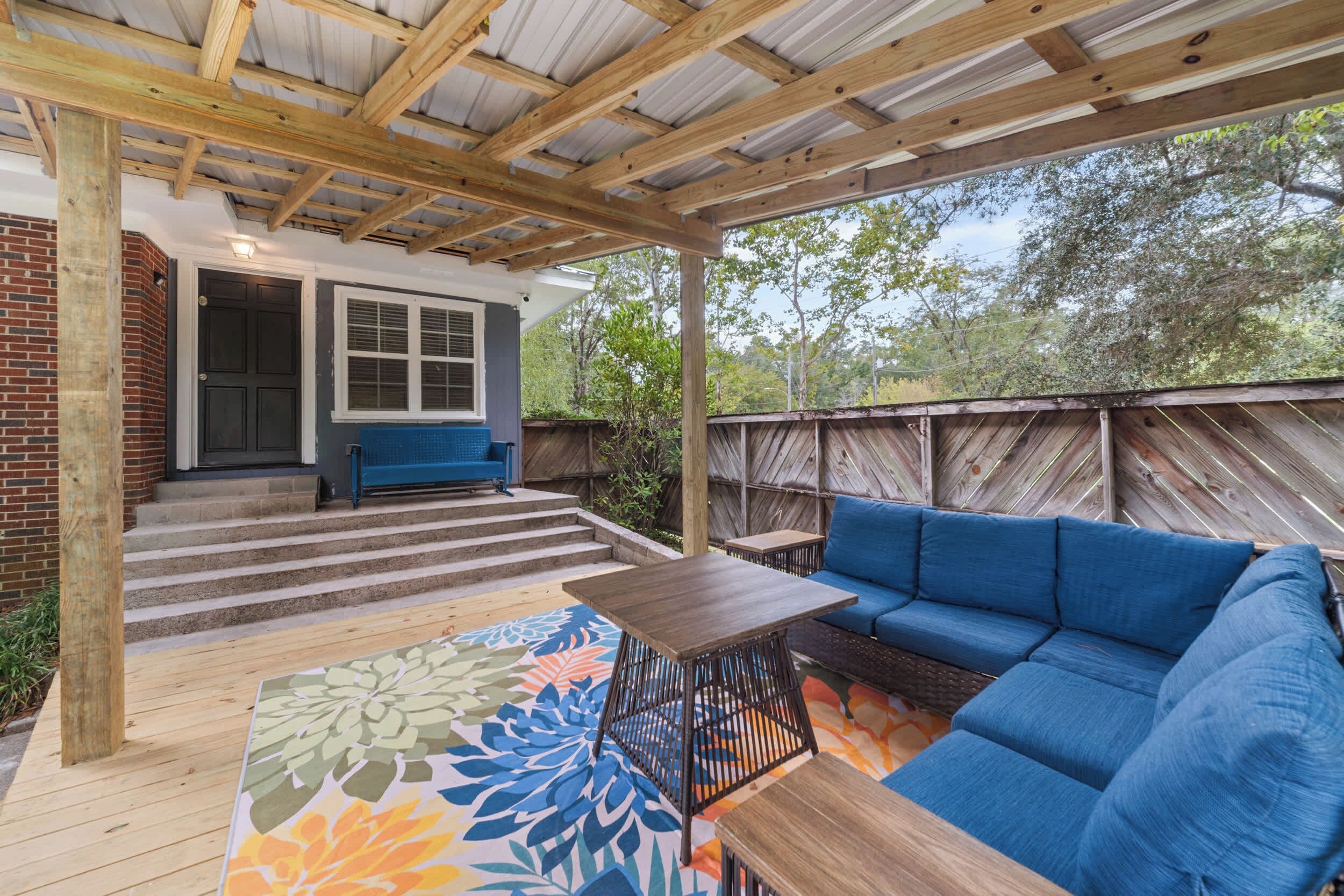 A covered patio with a wooden deck, a blue sofa, and a small table.