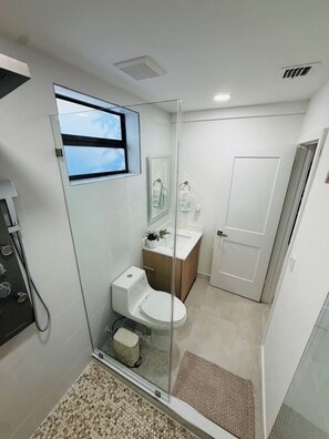 Un bagno moderno con doccia vetro, WC, lavandino e specchio.