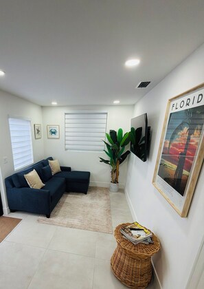 Uma sala de estar moderna com um sofá seccional, uma planta em vaso, um quadro e uma TV fixada na parede.
