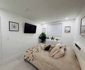 Ein Schlafzimmer mit einem Bett, einem Flachbildfernseher, einem Fenster mit Jalousien und Wandbildern.