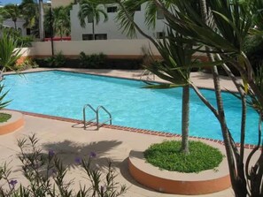 En swimmingpool med metalstige, omgivet af palmer og en murstenskant.