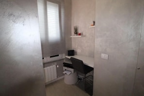 Een kleine kantoorruimte met een bureau, stoel en een plank.