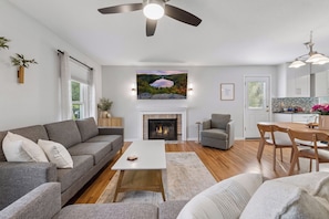 A modern living room with a fireplace, a dining area, and a kitchen with a view. - 4BR Chanhassen Home - 5-Min Walk to Dinner Theatre - Fire Pit (Chanhassen)
