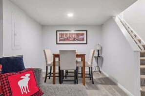 Een eetruimte met een tafel, stoelen, een lijst met afbeelding aan de muur, een lamp en een trap.
