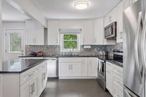 A modern kitchen with white cabinetry, a black countertop, stainless steel appliances, and a window with a view of greenery. - 4BR Chanhassen Home - 5-Min Walk to Dinner Theatre - Fire Pit (Chanhassen)
