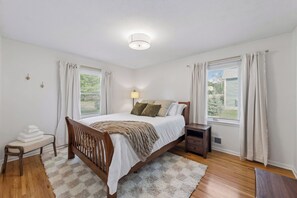 Ein Schlafzimmer mit einem hölzernen Bett, einem Nachttisch, einer Bank und einem Fenster mit Vorhängen.