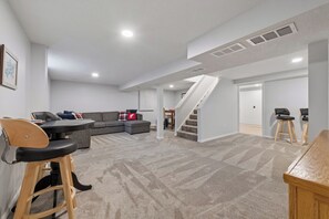 Ein geräumiger Wohnbereich mit einem grauen Sofa, einem Esstisch und einer Treppe, die zu einer weiteren Ebene führt.